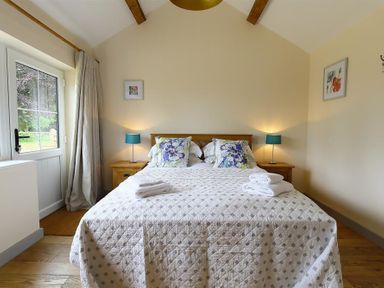 A bedroom with a double bed with patterned bedding two bedside tables with lamps and folded towels on the bed at Park Stables Wyck Beacon near Bourton on the Water