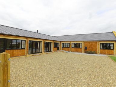 A courtyard with a gravel ground area surrounded by a wooden and stone building at Park Stables Wyck Beacon near Bourton-on-the-Water