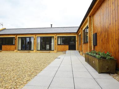 A gravel courtyard with wooden exterior walls and black framed windows at Park Stables Wyck Beacon near Bourton-on-the-Water