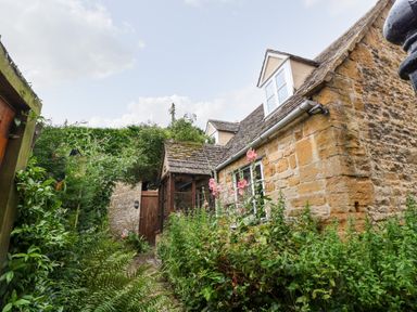 A stone cottage with a garden path surrounded by plants and flowers at Hadcroft Cottage in Aston Magna