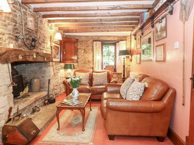 A sitting room with leather sofas a stone fireplace and wooden beams at Hadcroft Cottage in Aston Magna
