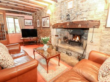 A sitting room with leather sofas a wooden coffee table and a fireplace at Hadcroft Cottage in Aston Magna