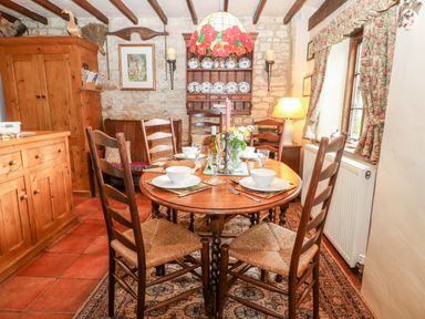 A dining room with a round wooden table set for four and wooden chairs at Hadcroft Cottage in Aston Magna