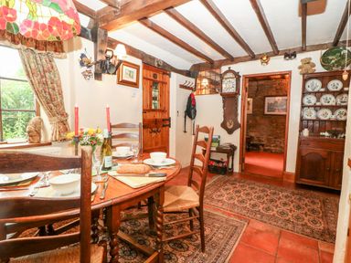 A dining room with a wooden table set for four and a grandfather clock at Hadcroft Cottage in Aston Magna