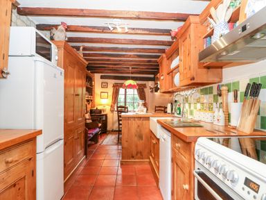 A kitchen with wooden cabinets tiled floor dining table and chairs at Hadcroft Cottage in Aston Magna