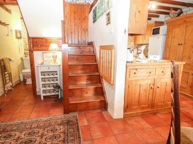 A kitchen area with wooden cabinets and stairs leading upstairs at Hadcroft Cottage in Aston Magna