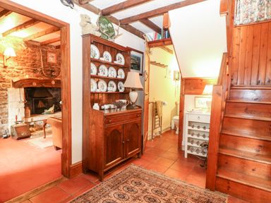 A hallway with wooden staircase and wooden cabinet with decorative plates next to a bathroom at Hadcroft Cottage in Aston Magna