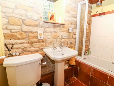 A bathroom with stone walls a pedestal sink a toilet and a bathtub at Hadcroft Cottage in Aston Magna