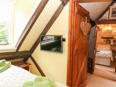 A bedroom with wooden beams a mounted television and a wooden door leading to another bedroom at Hadcroft Cottage in Aston Magna