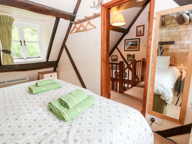 A bedroom with a bed with green towels on it a window with green curtains and a wooden staircase visible through a door at Hadcroft Cottage in Aston Magna