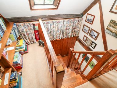 A wooden staircase with framed pictures on the wall and a bookshelf with board games at Hadcroft Cottage in Aston Magna