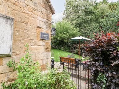 An outdoor garden area with a bench table umbrella and plants at Hadcroft Cottage in Aston Magna