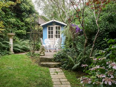 A garden with a blue shed white wrought iron table and chairs stone steps and various plants at Hadcroft Cottage in Aston Magna