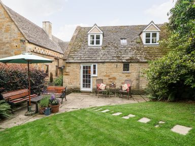 A garden with benches and chairs outside a stone cottage at Hadcroft Cottage in Aston Magna