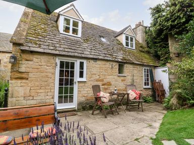 A stone cottage exterior with a tiled roof patio table and chairs and garden at Hadcroft Cottage in Aston Magna