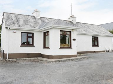 A single-story house with white walls and brown trim with multiple windows and two chimneys at Daffodil Cottage in Grange County Sligo