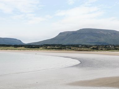 A sandy beach with water and mountains in the background at Daffodil Cottage in Grange County Sligo