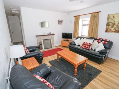 A living room with black leather sofas a wooden coffee table a fireplace and a television at Daffodil Cottage in Grange County Sligo