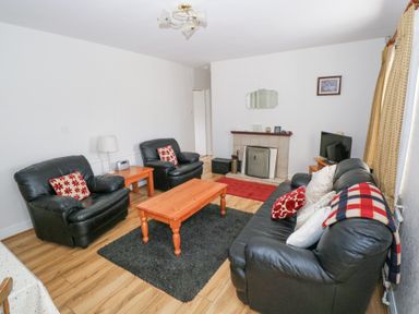 A living room with black leather sofas a wooden coffee table a fireplace and a television at Daffodil Cottage in Grange County Sligo