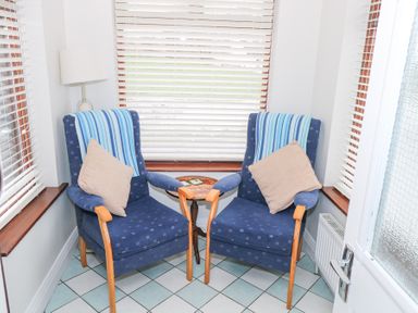 Two blue armchairs with wooden arms and beige pillows near a small round table and windows with white blinds at Daffodil Cottage in Grange County Sligo