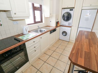A kitchen with white cabinets, wooden countertops, a stove, an oven, a sink below a window, a kettle, stacked washing machine and dryer, and a refrigerator at Daffodil Cottage in Grange County Sligo