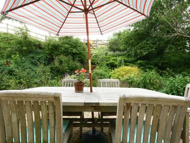 An outdoor wooden table and chairs with a striped umbrella and a potted plant in a garden at Cider Press Cottage Priston Village Bath