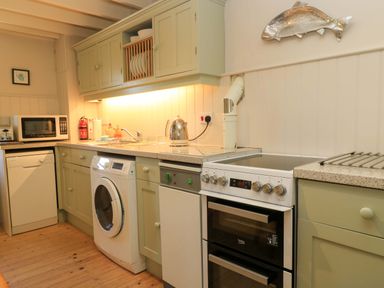 A kitchen with appliances including a washing machine and stove at Cider Press Cottage in Priston Village, Bath