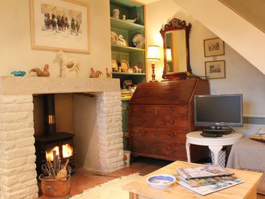 A living room with a fireplace a wooden dresser a television on a round table and shelves with dishes at The Mews Cottage in Tisbury