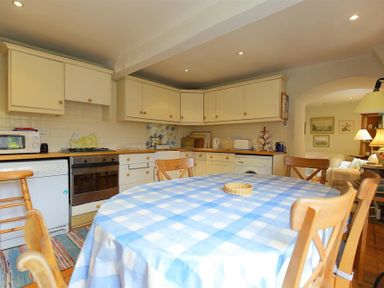A kitchen with cream cabinets a blue checkered tablecloth on a round table and wooden chairs at The Mews Cottage in Tisbury
