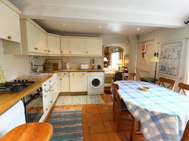 A kitchen with wooden countertops cabinets a washing machine and a dining table with a blue checkered tablecloth at The Mews Cottage in Tisbury