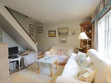 A living room with sofas a coffee table a television under stairs and framed pictures on walls at The Mews Cottage in Tisbury