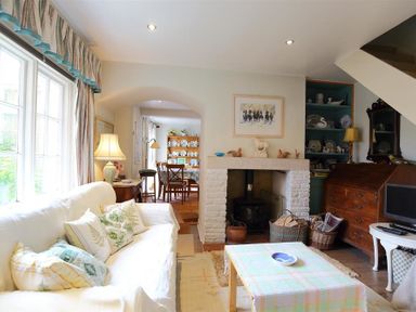 A living room with a white sofa pillows a wooden coffee table a fireplace and a dining area in the background at The Mews Cottage in Tisbury