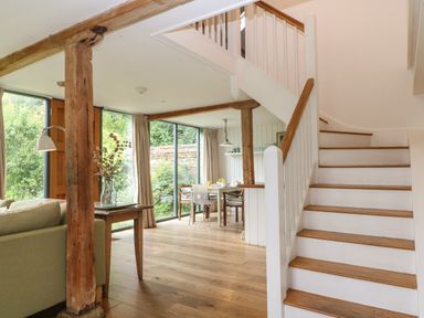 A dining area with a table and chairs next to large windows and a staircase with wooden steps at The Cart Barn in Ridge near Chilmark