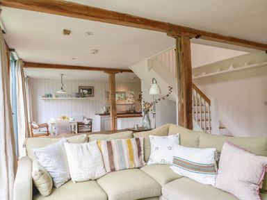A living room with a light green sectional sofa with pillows and wooden beams in an open space with a dining area and kitchen at The Cart Barn Ridge near Chilmark