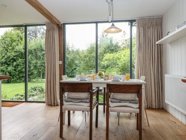 A dining area with a table set for breakfast in front of large glass windows overlooking a garden at The Cart Barn Ridge near Chilmark