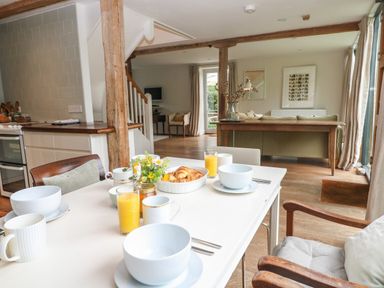 A dining table set with bowls, mugs, glasses of orange juice, croissants, and flowers in a kitchen and living area at The Cart Barn in Ridge near Chilmark