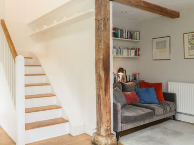 A staircase with wooden steps next to a living area with a gray sofa and shelves of books at The Cart Barn in Ridge near Chilmark