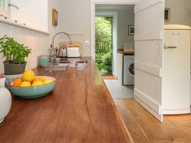 A kitchen countertop with a fruit bowl plants a toaster and a kettle with a view into a utility room and a garden at The Cart Barn in Ridge near Chilmark