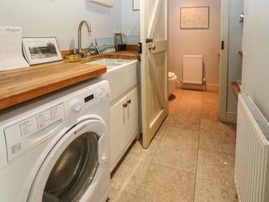 A utility room with washing machine wooden countertop and sink leading to a toilet at The Cart Barn in Ridge near Chilmark