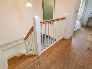A wooden staircase with white railing next to a hallway with wooden floor and a bedroom door at The Cart Barn in Ridge near Chilmark