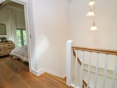 A staircase with wooden handrails and white balusters next to a bedroom with wooden floors and a chest of drawers at The Cart Barn in Ridge near Chilmark