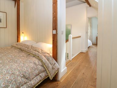 A bedroom with a patterned bedspread and wooden beams next to a hallway with wooden flooring and a white railing at The Cart Barn in Ridge near Chilmark