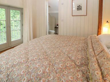 A bedroom with a patterned bedspread a bedside lamp a door to a bathroom and a set of glass double doors at The Cart Barn Ridge near Chilmark