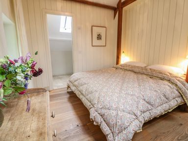 A bedroom with a double bed covered with a patterned comforter wooden floor a wooden dresser with flowers and a doorway leading to another room at The Cart Barn Ridge near Chilmark
