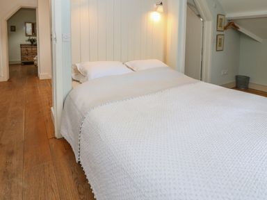 A bedroom with a double bed covered in a white quilt and pillows wooden floor and a doorway showing a dresser with flowers on it at The Cart Barn in Ridge near Chilmark