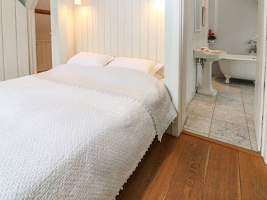 A bedroom with a bed covered with white bedding next to a bathroom with a pedestal sink and clawfoot tub at The Cart Barn in Ridge near Chilmark