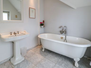 A bathroom with a freestanding clawfoot bathtub a pedestal sink and a small plant on a corner shelf at The Cart Barn in Ridge near Chilmark