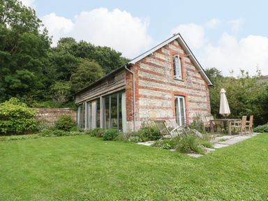 A garden with patio furniture and a small brick and stone house surrounded by trees at The Cart Barn Ridge near Chilmark