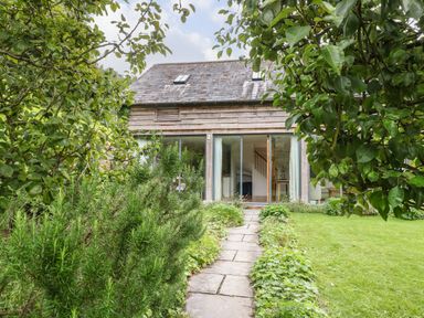 A garden path leading to a wooden house with large glass doors and skylights at The Cart Barn in Ridge near Chilmark
