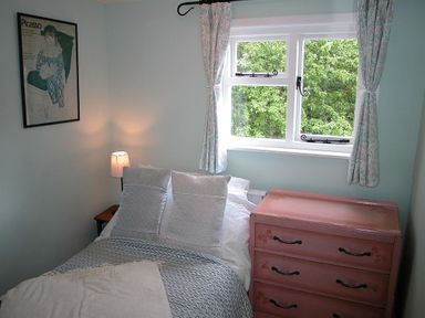 A bedroom with a bed next to a pink dresser under a window with curtains at Gun Hill Cottage in Heathfield